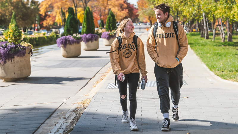 Two students wearing Purdue hoodies walking and talking.
